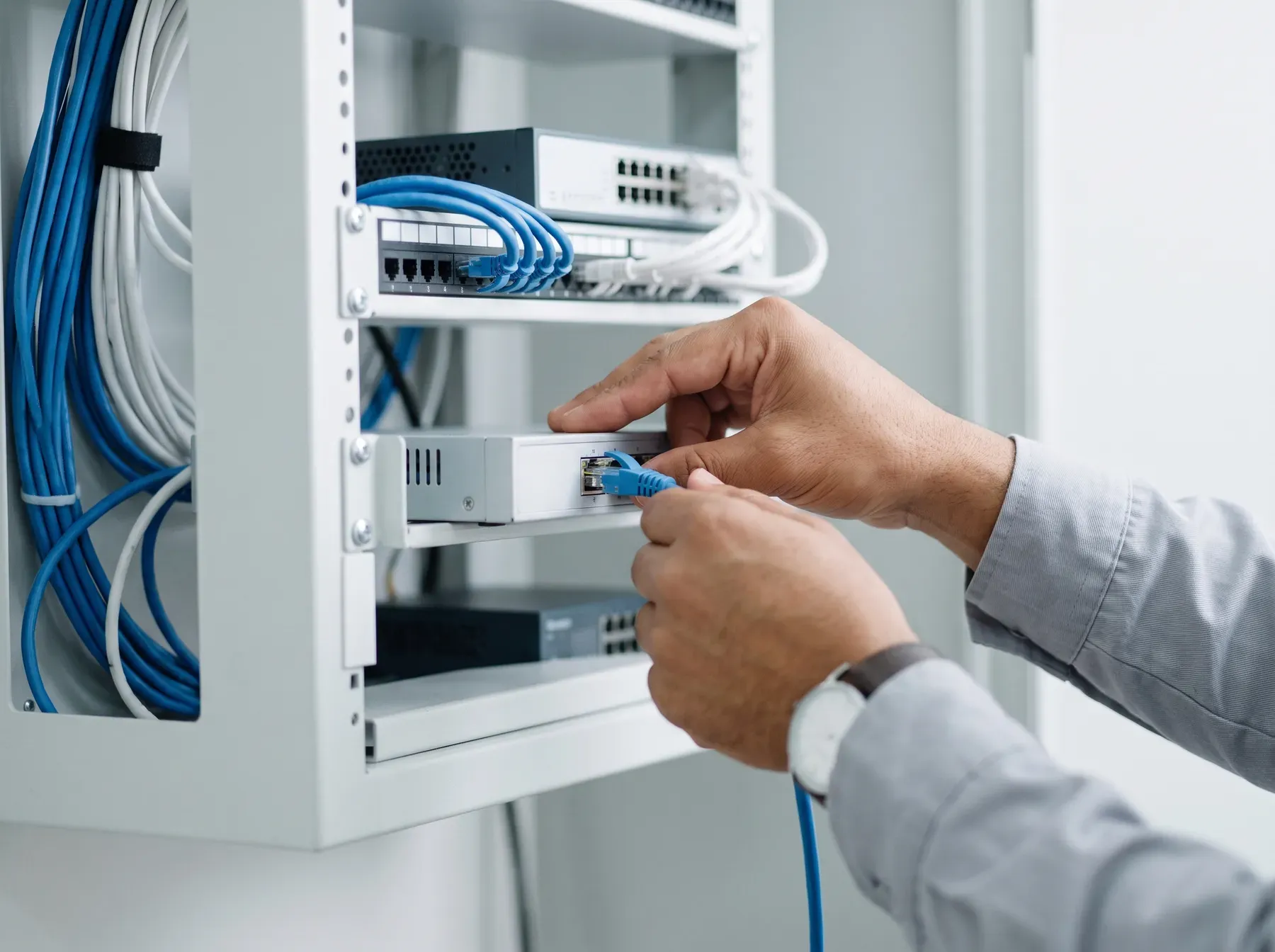 Manos de un agente de soporte conectando un cable de red a un equipo de seguridad en un cuarto de comunicaciones ordenado