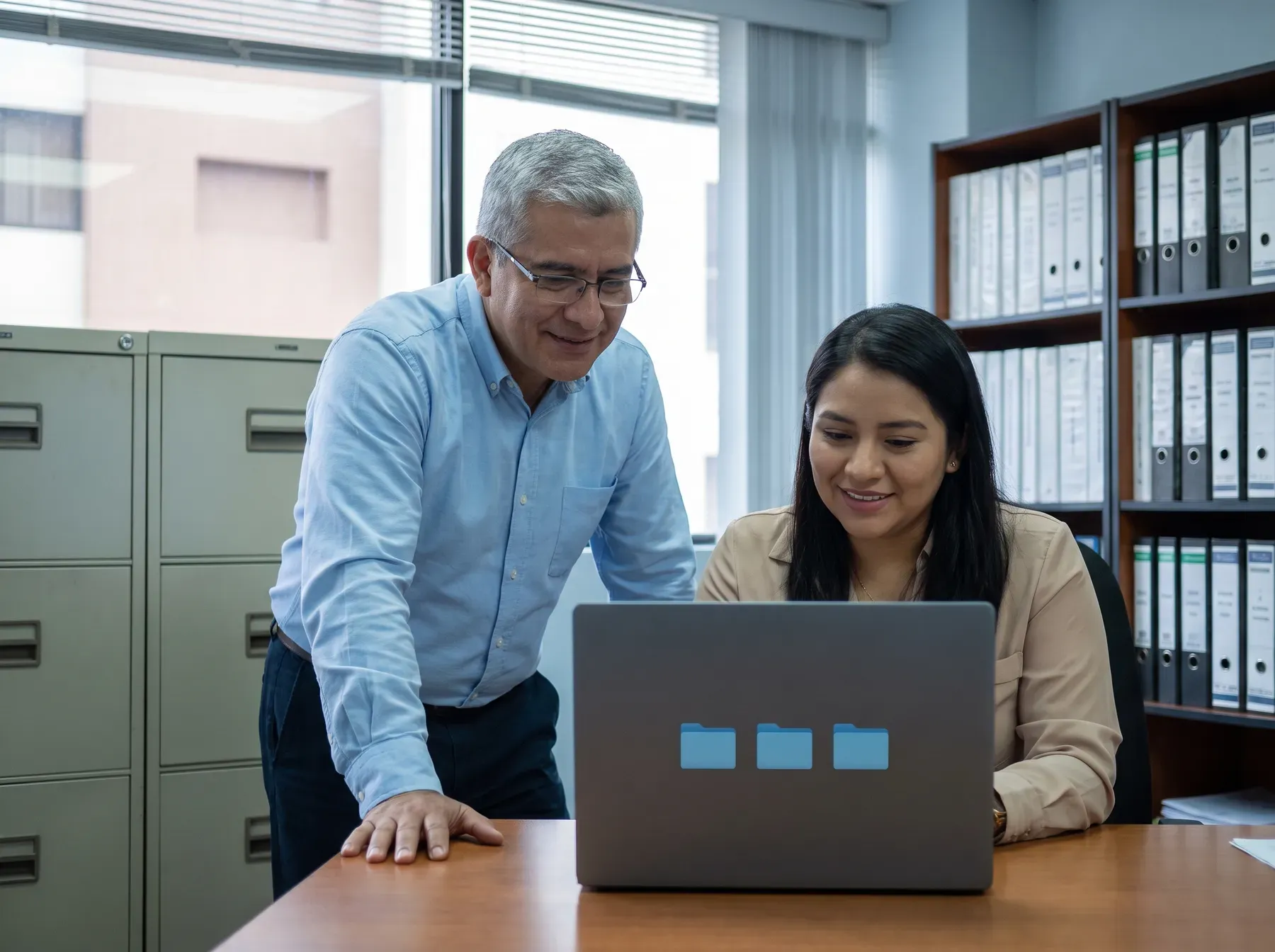 Dos colegas aliviados frente a una laptop tras recuperar un archivo importante en una oficina contable